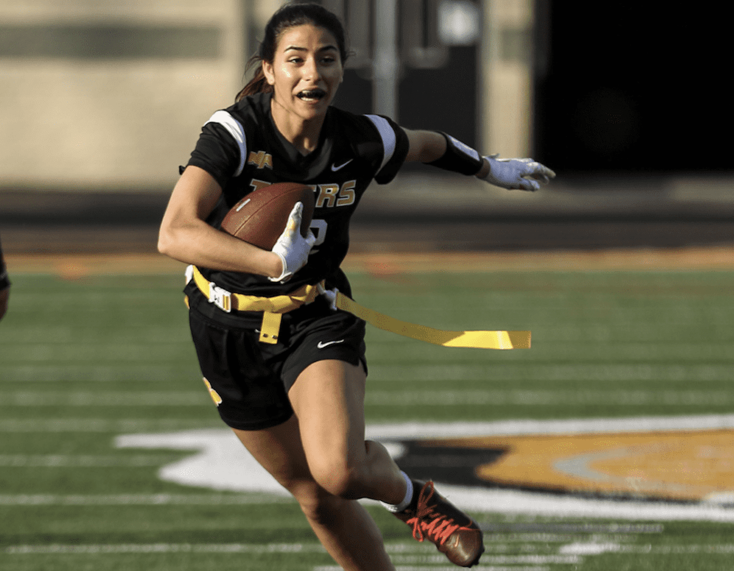 Female athlete running with a football on a field, showcasing speed and agility during a flag football game.