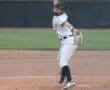 A young female softball player pitches on a field, focused and preparing to throw the ball to the batter.