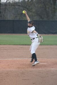 A young female softball player pitches on a field, focused and preparing to throw the ball to the batter.