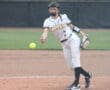 Female softball player pitching on a field, wearing a Tigers uniform with a ball in motion.