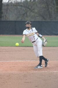 Female softball player pitching on a field, wearing a Tigers uniform with a ball in motion.