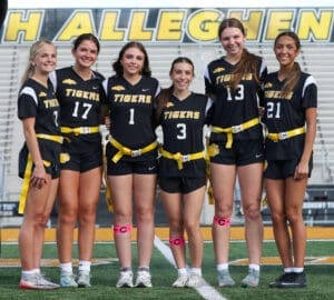 Six female athletes in black jerseys and yellow belts pose together on a sports field, showcasing team spirit for the Tigers.