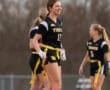 Cheerful female athlete in a flag football uniform, smiling on the field with teammates during practice.
