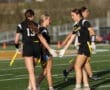 Female athletes in black uniforms strategizing during a flag football game on a sunny field. Teamwork in action!