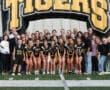 Girls' lacrosse team and supporters gather under a Tigers inflatable arch for a team photo at the stadium.