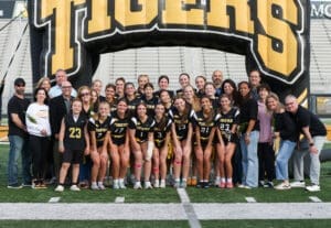 Girls' lacrosse team and supporters gather under a Tigers inflatable arch for a team photo at the stadium.