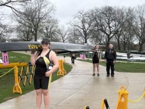Two rowers prepare their boat while a coach observes at a scenic riverside location, showcasing teamwork in rowing.