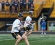 Two lacrosse players in action on the field, with spectators in the background, showcasing team spirit and athleticism.