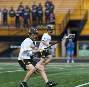Two lacrosse players in action on the field, with spectators in the background, showcasing team spirit and athleticism.