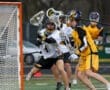 Lacrosse players in action as one goalie attempts to block a shot while teammates prepare for the play.