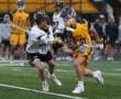 Two high school lacrosse players compete for the ball during a rainy game on a turf field.