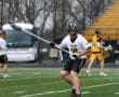 Lacrosse player in action on field, wearing a Tigers jersey, preparing to pass or shoot in a rainy match.