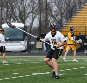 Lacrosse player in action on field, wearing a Tigers jersey, preparing to pass or shoot in a rainy match.
