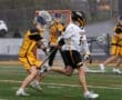 Two lacrosse players compete on a rainy field, showcasing athletic skill and teamwork during a competitive match.