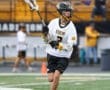 Lacrosse player in action wearing a Tigers jersey, dribbling on the field with spectators in the background.