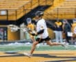 Young lacrosse player in action during a practice session on a field with yellow and black markings, teammates in background.