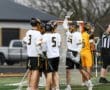 Lacrosse players celebrate a goal during a match on a turf field, showcasing teamwork and sportsmanship.