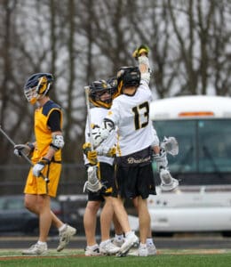 Teenage lacrosse players celebrate a goal during a match, showcasing teamwork and sportsmanship on the field.
