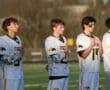 Lacrosse players in jerseys stand attentively during the national anthem on the field. Team spirit and unity on display.