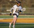 Lacrosse player wearing a Tigers jersey runs on the field, holding a stick during a competitive match.