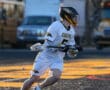 Lacrosse player in a white Tigers uniform sprinting on the field, carrying a lacrosse stick in a dynamic action pose.