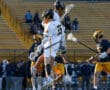 Lacrosse players jumping to celebrate during a game, showcasing teamwork and athleticism on the field.