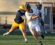 Lacrosse players in action, one dodging a tackle while the other attempts to maintain possession of the ball.