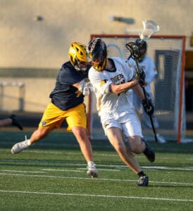 Lacrosse players in action, one dodging a tackle while the other attempts to maintain possession of the ball.