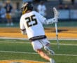 Lacrosse player wearing jersey number 25, sprinting on a field with Brotherhood on his shorts, focused on the game.