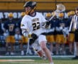 Lacrosse player in action, number 22, wearing white jersey and helmet, preparing to shoot on the field during a game.