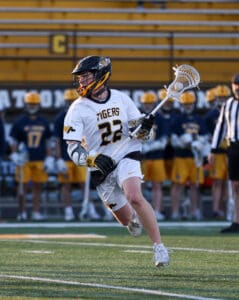 Lacrosse player in action, number 22, wearing white jersey and helmet, preparing to shoot on the field during a game.