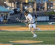 Lacrosse player in action on the field, wearing a white jersey, running with a stick, showcasing athleticism and teamwork.