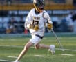 Lacrosse player in a white Tigers uniform running with a stick on the field during a game.