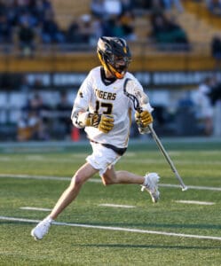 Lacrosse player in a white Tigers uniform running with a stick on the field during a game.