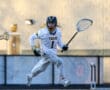 Lacrosse player in a white Tigers jersey sprints across the field, stick in hand, ready to make a play.