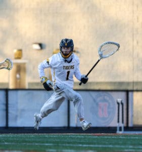 Lacrosse player in a white Tigers jersey sprints across the field, stick in hand, ready to make a play.