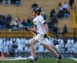 Lacrosse player in action, running on the field with a stick, during a game in front of cheering spectators.