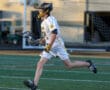 Lacrosse player in a white jersey runs on the field, stick in hand, ready for the game action.