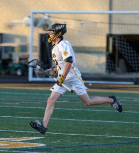Lacrosse player in a white jersey runs on the field, stick in hand, ready for the game action.