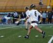 Lacrosse player in action, wearing number 6, running on the field with a stick during a game.