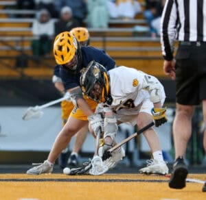 Two lacrosse players compete for the ball during a game, showcasing intensity and athleticism on the field.