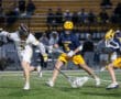 Two high school lacrosse players compete for the ball during a night game on a well-lit field.