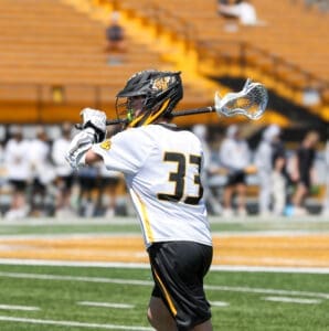 Young lacrosse player in action, wearing jersey number 33, practicing on a sunny field during a game.