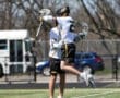 Two lacrosse players celebrating a victory by jumping in the air on a sunny field.