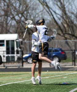 Two lacrosse players celebrating a victory by jumping in the air on a sunny field.