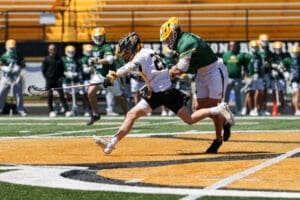 Two lacrosse players compete for the ball on a sunny field, showcasing athleticism and teamwork during a game.