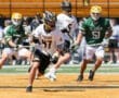 High school lacrosse players in action on a field, with teams in black and green jerseys competing.