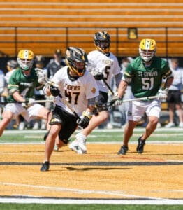 High school lacrosse players in action on a field, with teams in black and green jerseys competing.