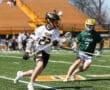 Two young lacrosse players compete on a sunny field, one in a white Tigers jersey and the other in a green St. Edward jersey.