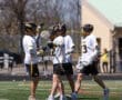 Lacrosse players celebrate a goal on the field, showcasing teamwork and athleticism during a sunny day.